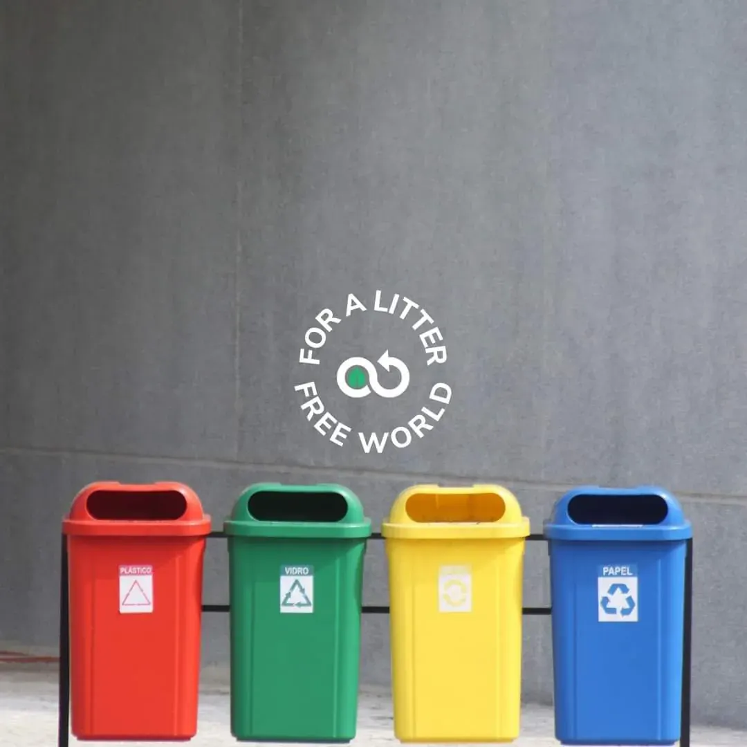 Four labeled recycling bins in front of a wall with a circular logo reading 'FOR A LITER FREE WORLD' at a local recycling center